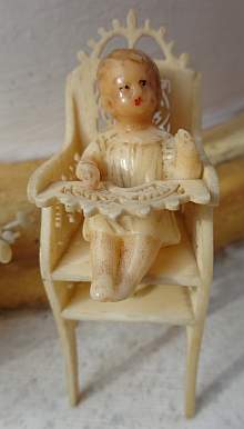 Antiker Kinderstuhl mit kleiner Babywachspuppe.